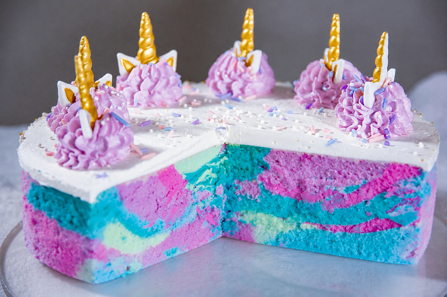 A rainbow swirled marshmallow birthday cake topped with piped unicorn swirls and gold horns