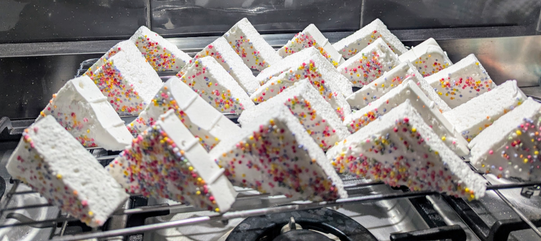 Triangles of fairy bread marshmallow coated in hundreds and thousands on a cooling rack