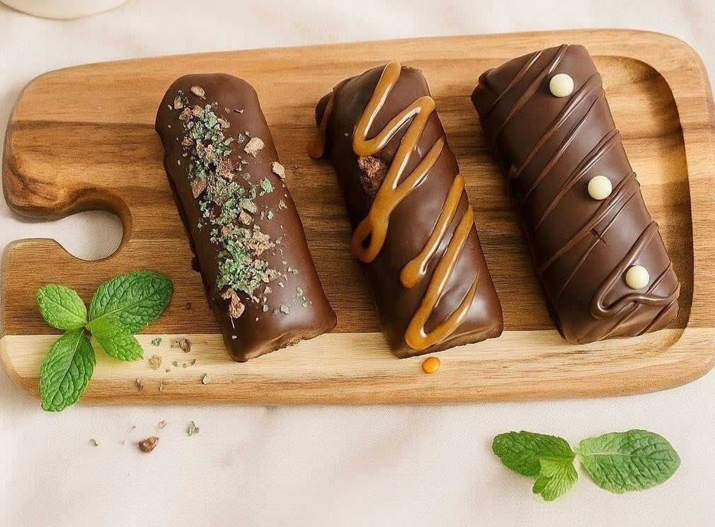 Three chocolate coated mallow logs with mint, caramel and white chocolate finishes on a wooden board