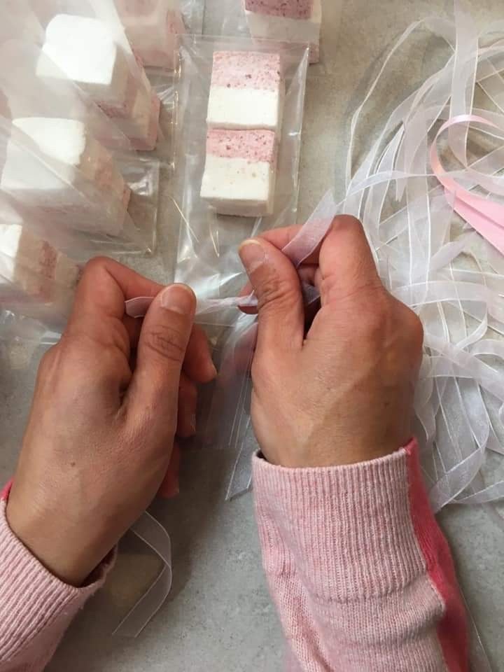 Hands tying organza ribbon around individually wrapped pink and white marshmallow wedding favours
